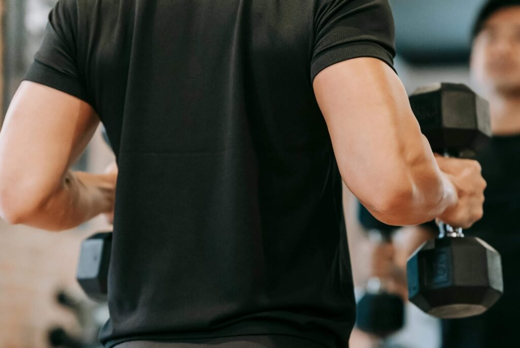 Close-up of a person holding dumbbells in a gym, focusing on arm muscles