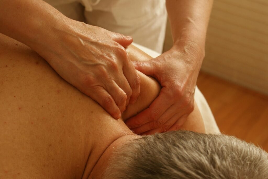 Close-up of a massage therapist's hands applying firm pressure to the shoulder and upper back of an old man  
