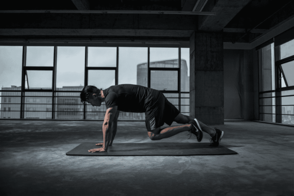 A man performing a mountain climber exercise on a mat in a modern industrial gym, following a training program