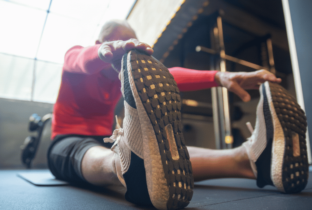 An old man doing seated toe touch exercise in the gym