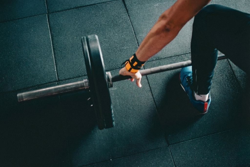High-angle view of an athlete’s arm reaching down to grip a loaded barbell on a gym floor