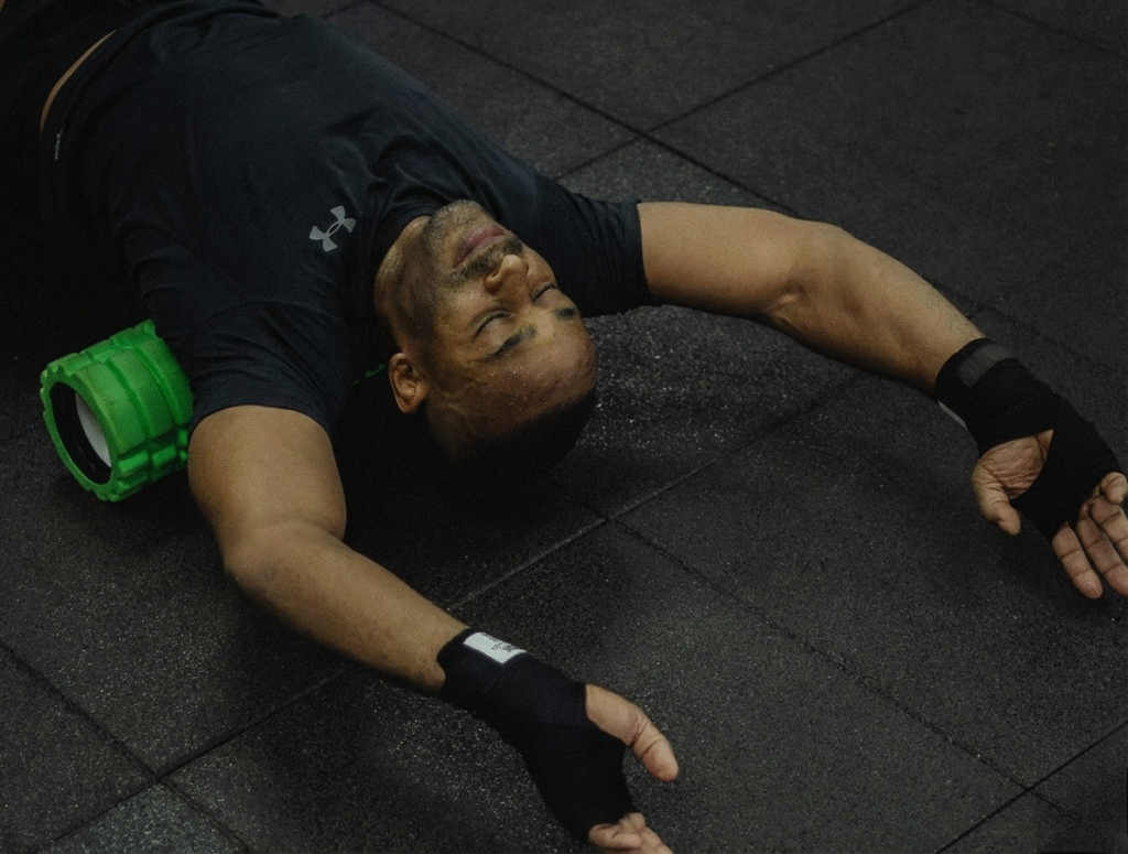 A person using a foam roller in a gym setting, lying on the floor with arms extended