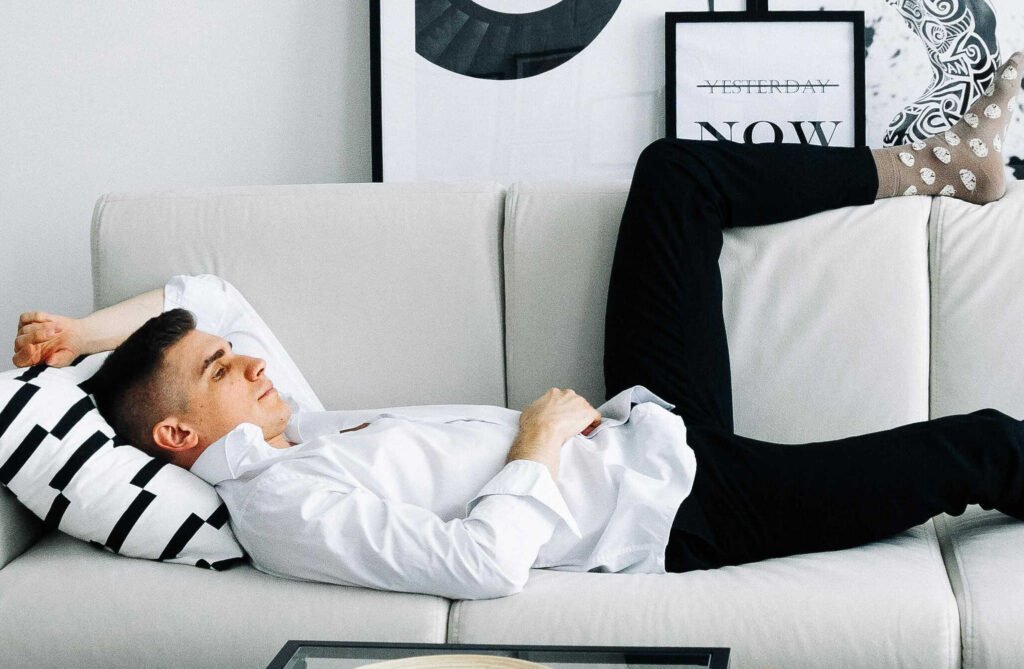 A man reclining on a gray sofa with a black and white mixed cushion